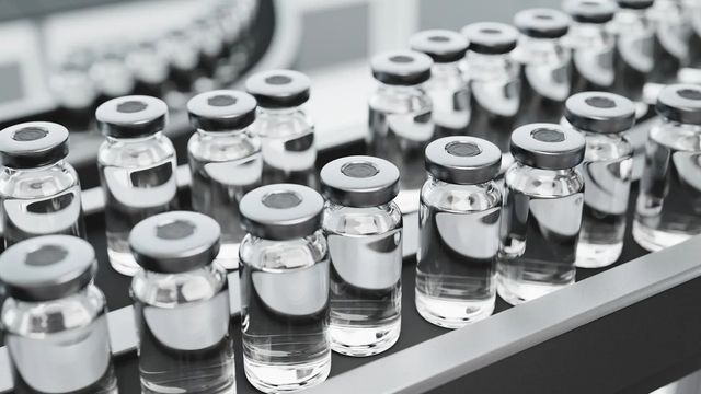 Clear glass vials filled with a colourless liquid sit on a conveyor belt.