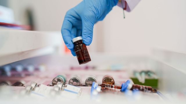 A person in a blue glove holding a vial for medical testing and analysis.