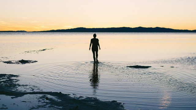 Silhouette of person standing in the shallows of a lake.