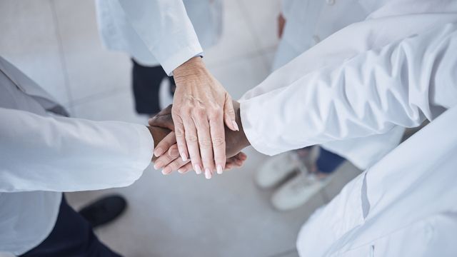 A group of scientists in lab coats putting there hands together to represent teamwork and unity. 