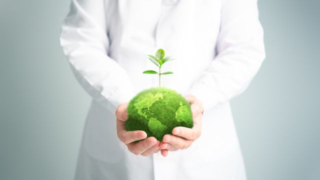 Someone wearing a lab coat holding a ball of earth.