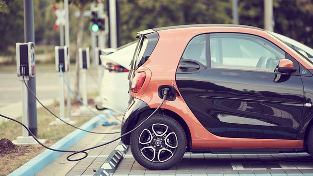 Orange and black electric car plugged into a charging point in a car park.