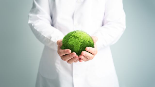 Someone in a lab coat holding a green sphere that resembles the earth.